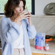 Une femme en périménopause dans sa ciusine boit la boisson calmante et digestive Nuit paisible de Joïsta, dans une tasse, et prend des gélules aura zen de Joïsta.